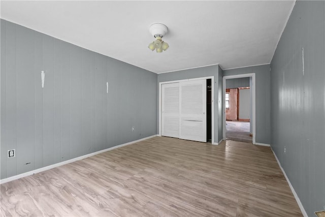 unfurnished bedroom featuring wooden walls, a closet, and light hardwood / wood-style flooring