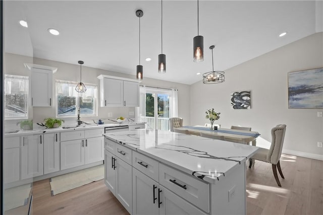 kitchen with vaulted ceiling, a kitchen island, pendant lighting, light hardwood / wood-style floors, and white cabinetry