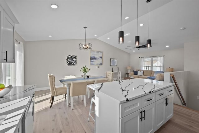 kitchen with light wood-type flooring, ceiling fan, white cabinets, a kitchen island, and hanging light fixtures