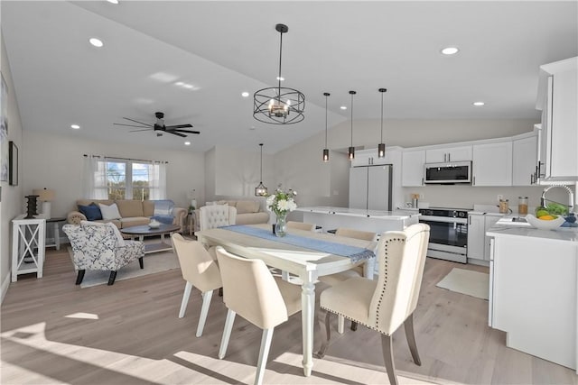 dining space with lofted ceiling, light hardwood / wood-style flooring, ceiling fan with notable chandelier, and sink