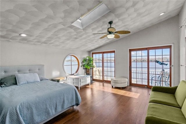 bedroom featuring access to exterior, vaulted ceiling with skylight, ceiling fan, a water view, and hardwood / wood-style flooring