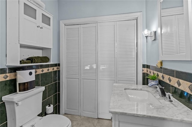 bathroom with tile patterned flooring, vanity, toilet, and tile walls