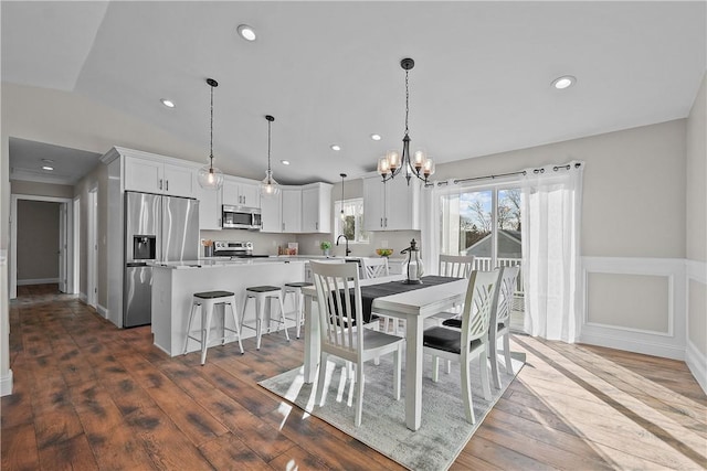 dining area featuring dark wood-type flooring, vaulted ceiling, a notable chandelier, and sink