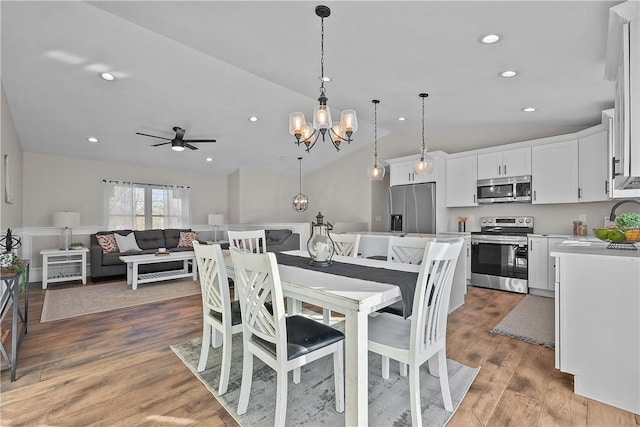 dining room with ceiling fan with notable chandelier, light hardwood / wood-style floors, vaulted ceiling, and sink