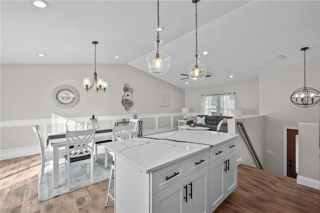 kitchen featuring light stone countertops, a center island, pendant lighting, white cabinets, and hardwood / wood-style flooring