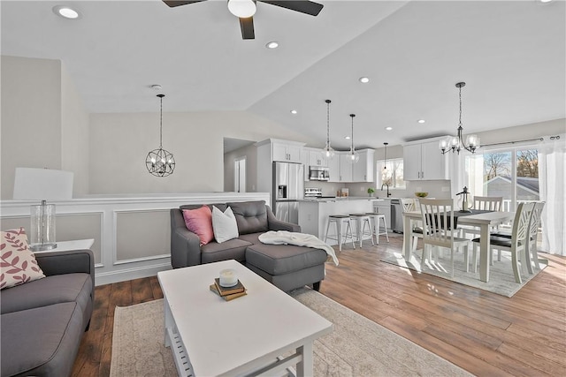 living room with vaulted ceiling, sink, wood-type flooring, and ceiling fan with notable chandelier