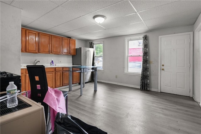 kitchen with a paneled ceiling, light wood-type flooring, stainless steel refrigerator, and black / electric stove