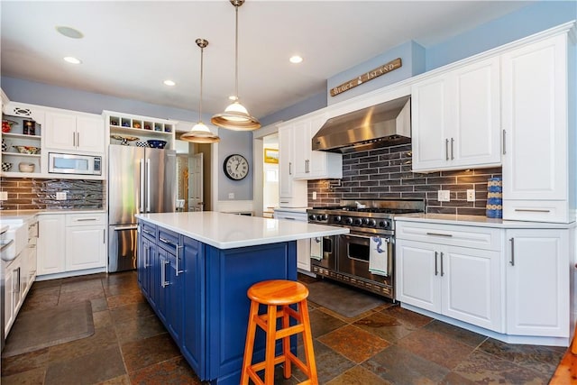 kitchen with backsplash, wall chimney range hood, hanging light fixtures, blue cabinetry, and appliances with stainless steel finishes