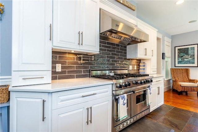 kitchen featuring white cabinets, tasteful backsplash, range with two ovens, and wall chimney range hood