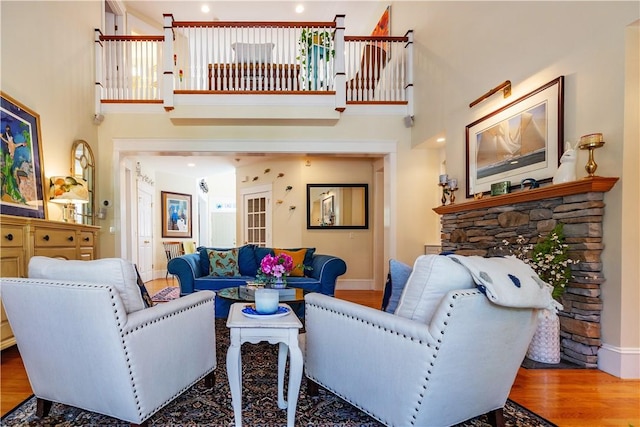 living room with hardwood / wood-style floors, a stone fireplace, and a high ceiling