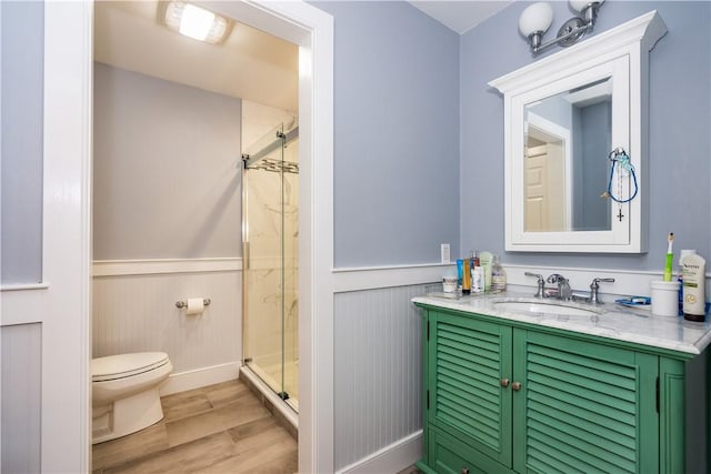 bathroom featuring a shower with door, vanity, wood-type flooring, and toilet