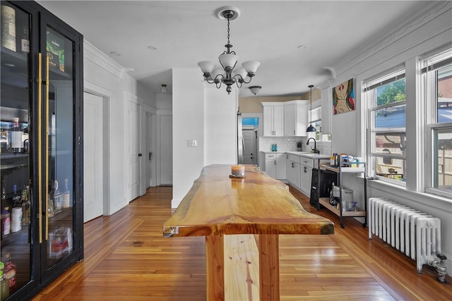 dining room with radiator, sink, a chandelier, and light wood-type flooring