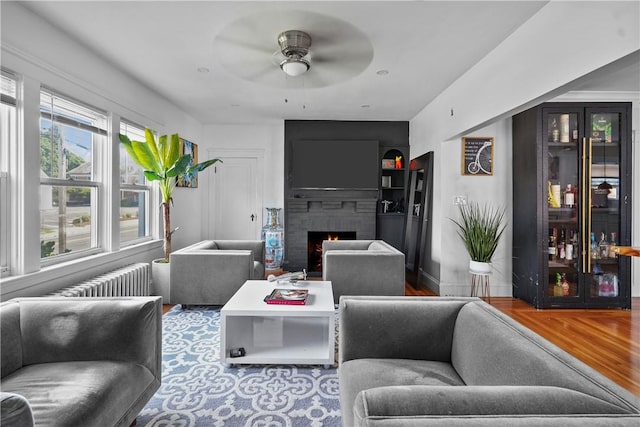 living room featuring ceiling fan, a large fireplace, wood-type flooring, and built in features