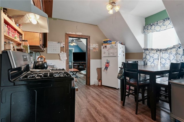 kitchen featuring exhaust hood, vaulted ceiling, light hardwood / wood-style flooring, black gas range oven, and white fridge