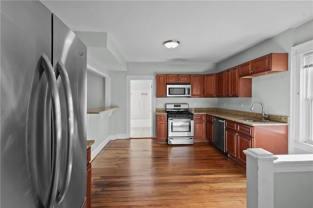 kitchen with a wealth of natural light, sink, light stone counters, wood-type flooring, and appliances with stainless steel finishes