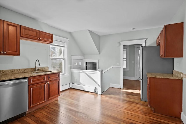 kitchen with light stone countertops, sink, stainless steel appliances, light hardwood / wood-style flooring, and a baseboard heating unit