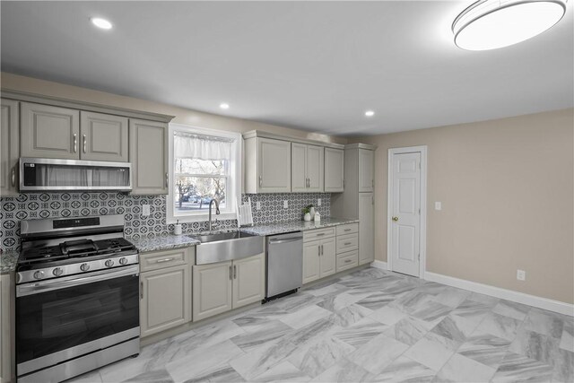 kitchen with gray cabinetry, light stone counters, sink, and appliances with stainless steel finishes