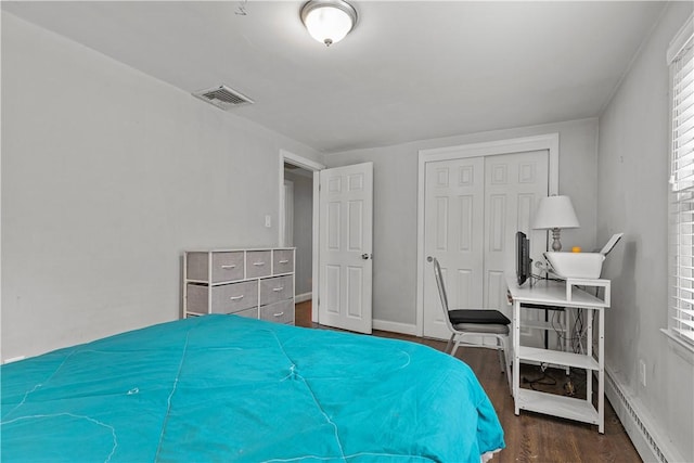 bedroom with dark hardwood / wood-style flooring, baseboard heating, and a closet