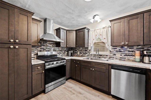 kitchen featuring dark brown cabinetry, sink, wall chimney range hood, and appliances with stainless steel finishes