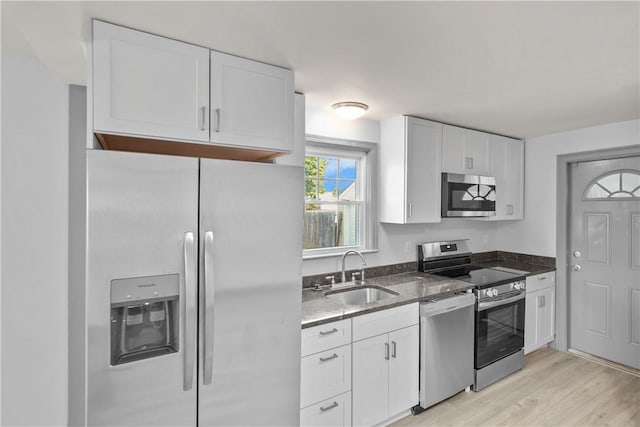 kitchen with white cabinets, sink, dark stone countertops, light wood-type flooring, and stainless steel appliances