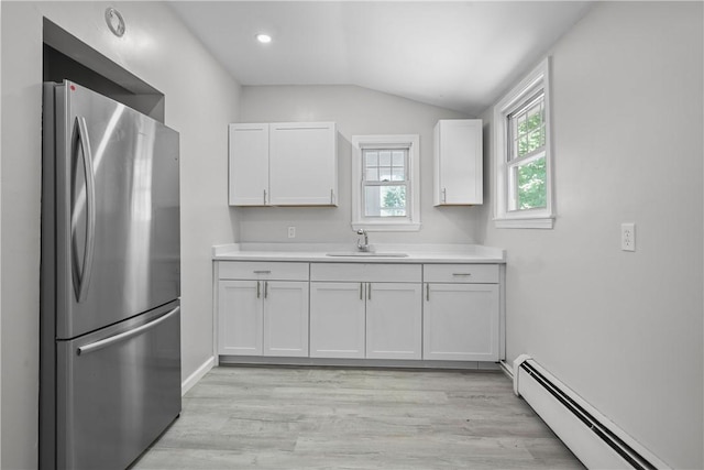 kitchen with white cabinets, sink, vaulted ceiling, stainless steel fridge, and baseboard heating