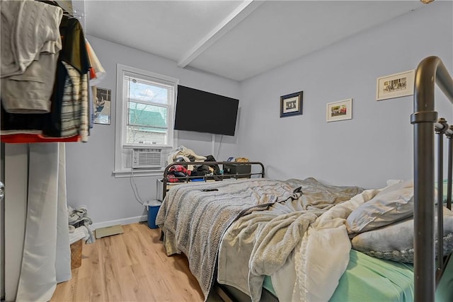 bedroom featuring cooling unit, beamed ceiling, and light wood-type flooring