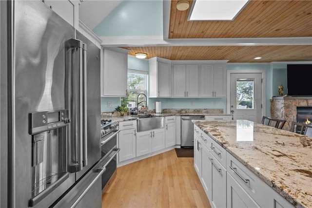 kitchen with wooden ceiling, white cabinets, a stone fireplace, a wealth of natural light, and appliances with stainless steel finishes