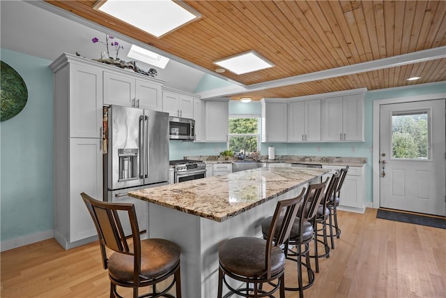 kitchen with a center island, white cabinets, a skylight, appliances with stainless steel finishes, and wood ceiling