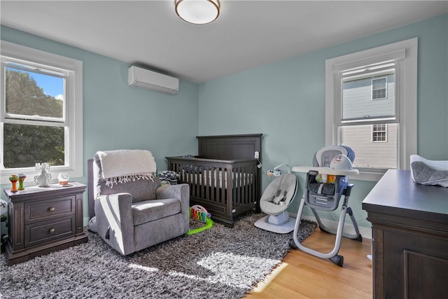 bedroom with hardwood / wood-style floors, a wall unit AC, and a nursery area