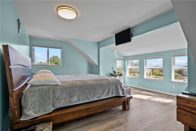 bedroom with vaulted ceiling, light wood-type flooring, and multiple windows