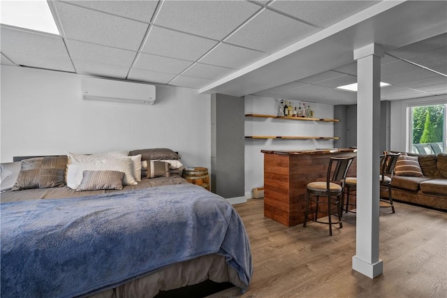 bedroom featuring wood-type flooring, a paneled ceiling, and a wall unit AC