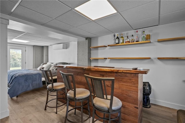 bar with a paneled ceiling, light hardwood / wood-style floors, and an AC wall unit