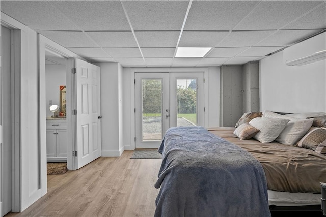 bedroom with a wall mounted AC, french doors, light hardwood / wood-style flooring, and a drop ceiling