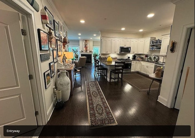 kitchen featuring dark wood-type flooring, a breakfast bar area, a fireplace, white cabinets, and appliances with stainless steel finishes