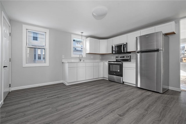 kitchen featuring hanging light fixtures, dark hardwood / wood-style flooring, white cabinets, appliances with stainless steel finishes, and sink