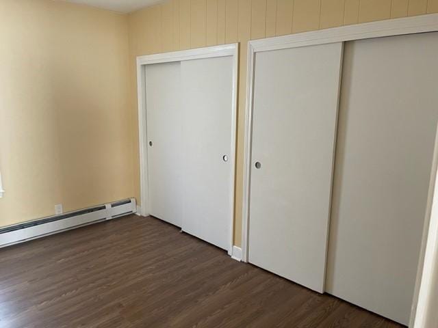 unfurnished bedroom with baseboard heating and dark wood-type flooring