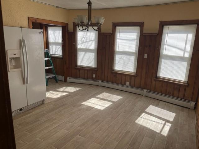 unfurnished dining area with wooden walls, plenty of natural light, a chandelier, and a baseboard heating unit