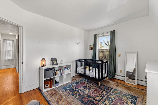 bedroom featuring a crib, wood-type flooring, and a baseboard radiator