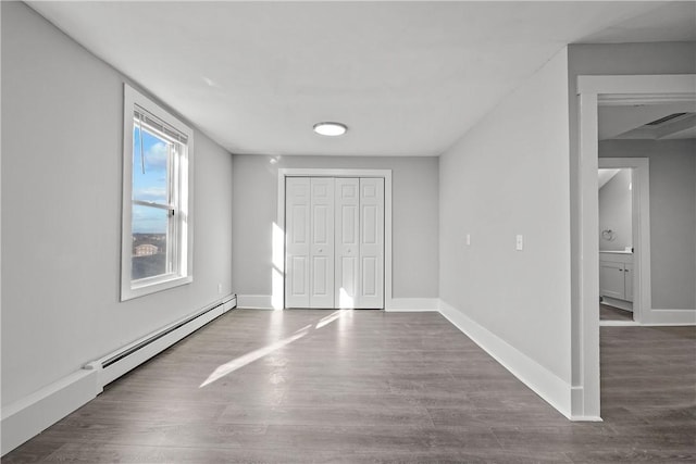 unfurnished bedroom featuring a closet, dark hardwood / wood-style floors, and a baseboard heating unit