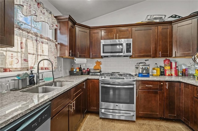 kitchen with decorative backsplash, light stone counters, stainless steel appliances, vaulted ceiling, and sink