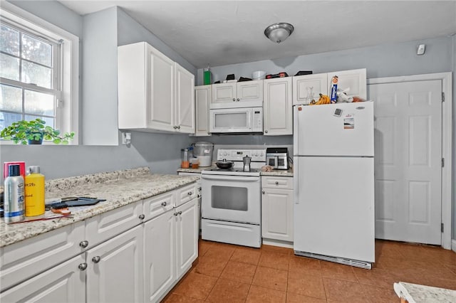 kitchen with white cabinetry, light tile patterned floors, light stone counters, and white appliances