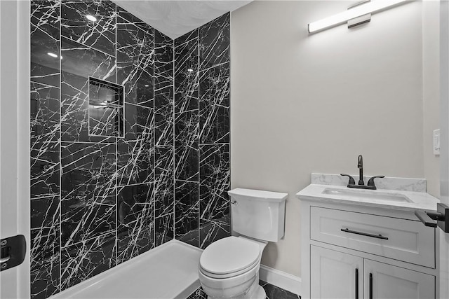 bathroom with a tile shower, vanity, and toilet