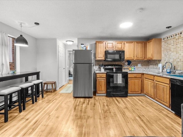 kitchen featuring sink, hanging light fixtures, light hardwood / wood-style flooring, decorative backsplash, and black appliances