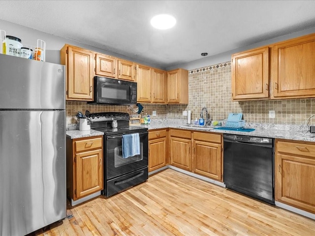 kitchen with sink, light stone counters, light hardwood / wood-style floors, decorative backsplash, and black appliances