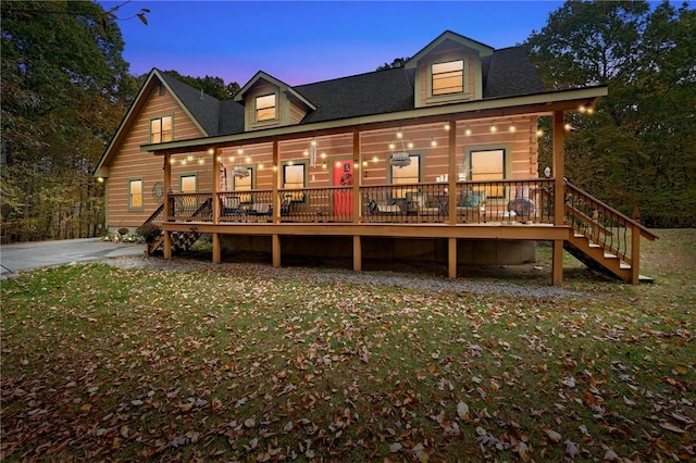 back house at dusk featuring a lawn and a porch