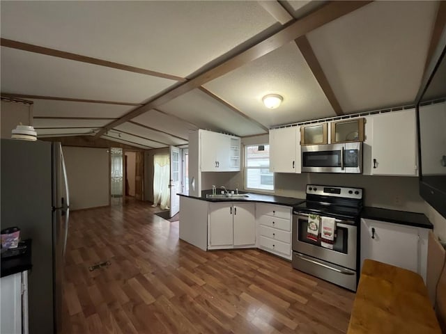 kitchen with sink, dark wood-type flooring, stainless steel appliances, vaulted ceiling, and white cabinets