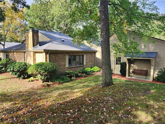 view of front of property with a front lawn, brick siding, a patio, and a chimney
