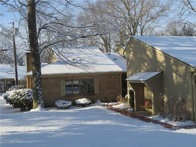 snow covered property with brick siding