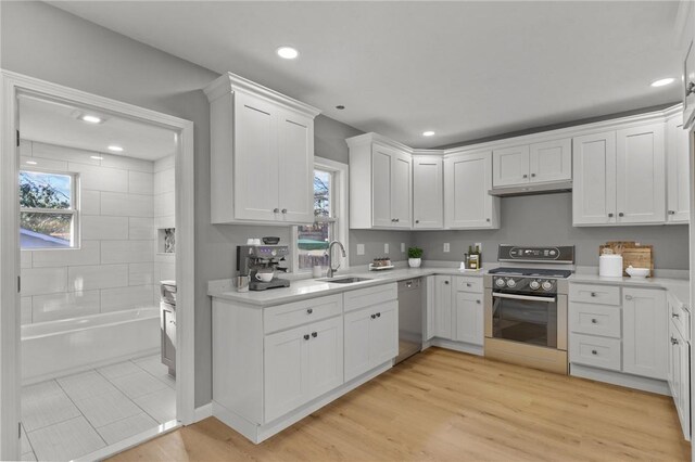 kitchen featuring stainless steel dishwasher, sink, light hardwood / wood-style flooring, range, and white cabinetry