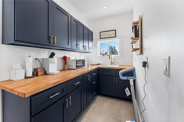 kitchen with butcher block countertops, blue cabinetry, decorative backsplash, and sink